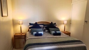 A neatly made bed with striped bedding and multiple pillows, two bedside tables with lamps, and a door in the background. - 39B Club Mykonos (eMdloti)