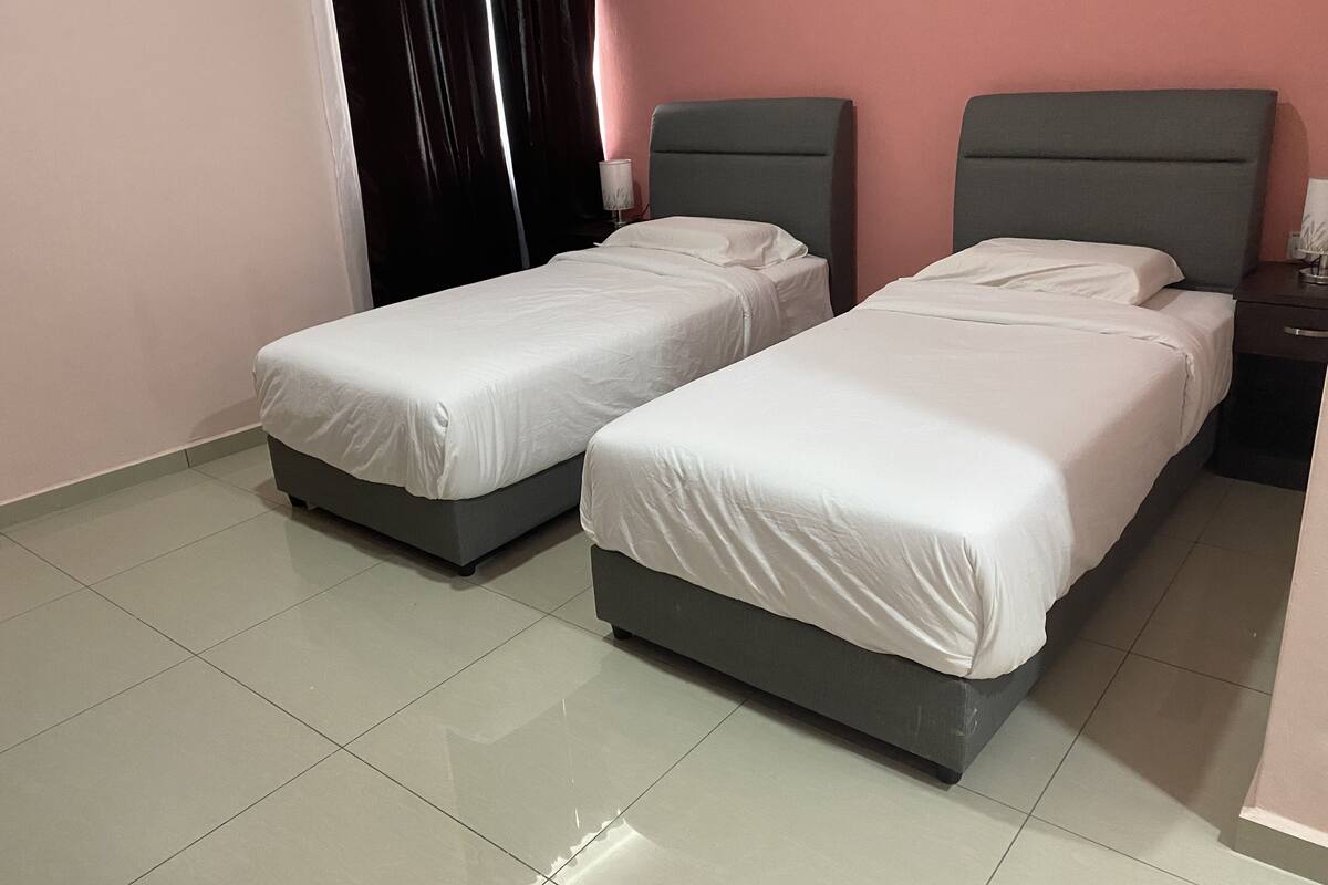 Dos camas individuales con cabeceras grises en una habitación con paredes rosadas y suelo de baldosas.