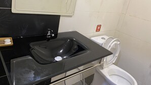Un baño con un lavabo negro, un inodoro y un espejo sobre el lavabo.