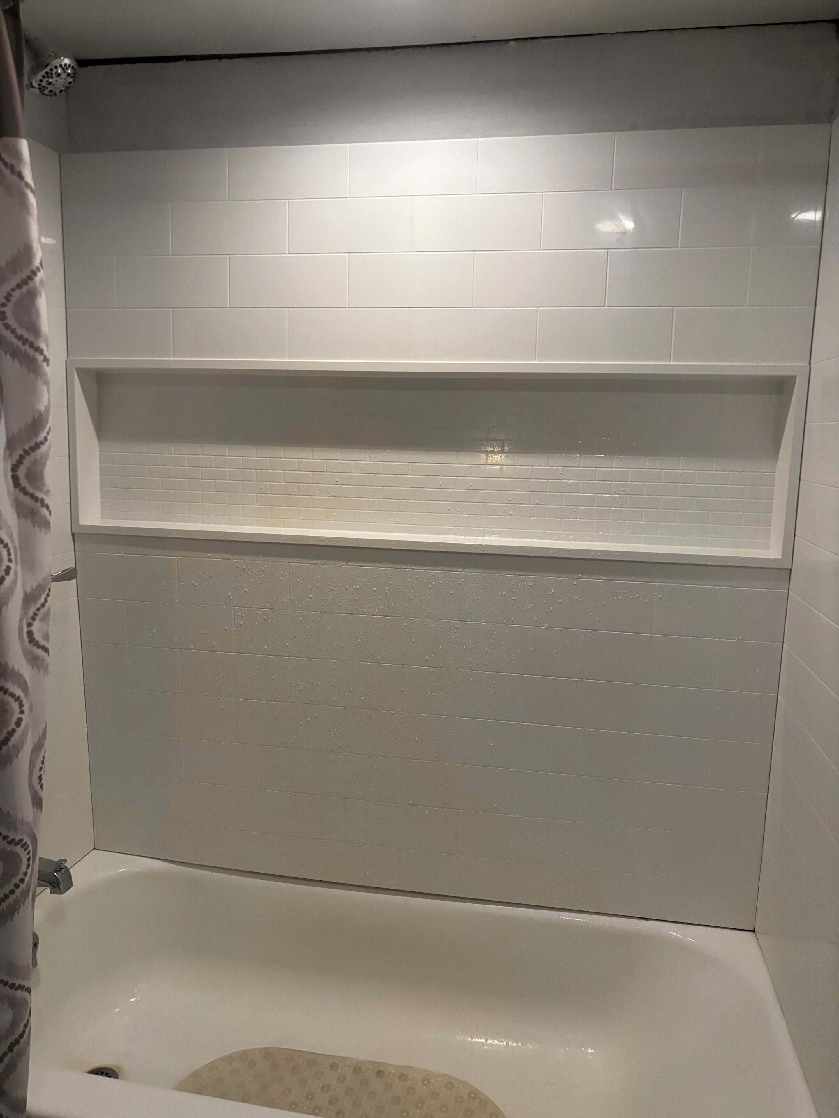 Une salle de bain avec une baignoire, un espace douche et une étagère au-dessus de la baignoire.