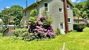A two-story house with a chimney, surrounded by lush greenery and a small garden with purple flowers. - Score The perfect Summer Winter getaway: Lakeside retreat for your winning team  (Maryland)