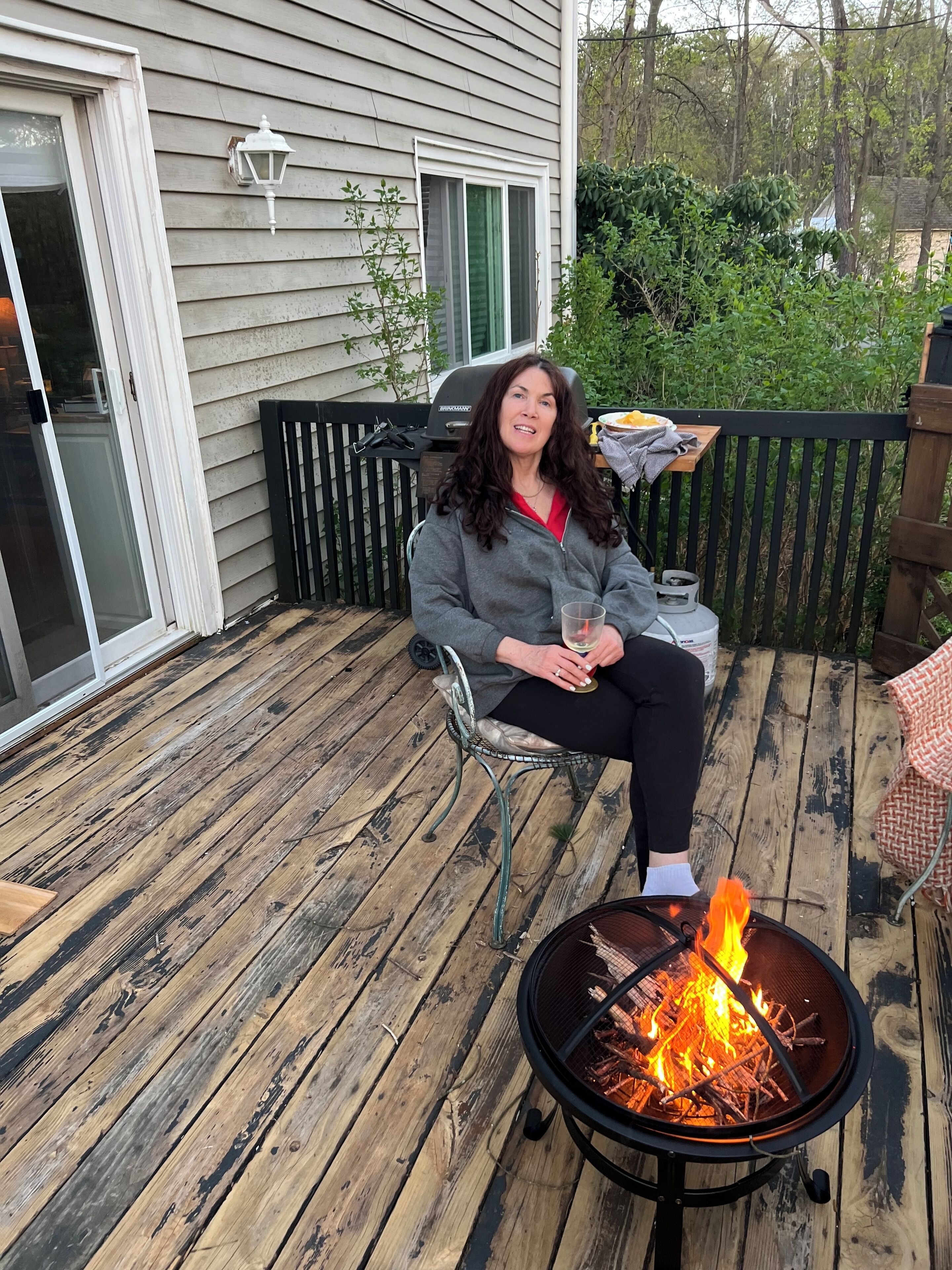 A person sitting on a chair on a wooden deck with a fire pit in front.
