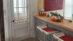 A room with a white door, a window with blinds, a red abstract painting, a wooden countertop, and two white bar stools. - Score The perfect Summer Winter getaway: Lakeside retreat for your winning team  (Maryland)