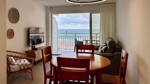 Un salon moderne comprenant un coin repas, un téléviseur et un balcon avec vue sur la mer.