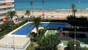 Vue d’une plage avec une piscine et un court de tennis, le tout entouré d’un bâtiment doté de balcons.