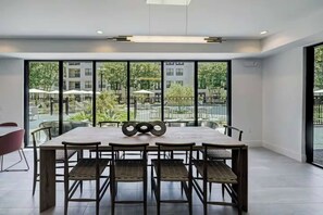 A modern dining area with a large table and chairs, large windows with a view of greenery and buildings, and a clean, minimalist design.