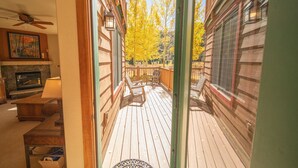 A wooden deck with a fireplace, a ceiling fan, and a view of trees. - Red Hawk Townhomes 2345 (Keystone)