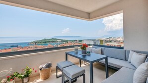 Uma varanda com sofá, uma mesa pequena e vista para o mar e a paisagem urbana.