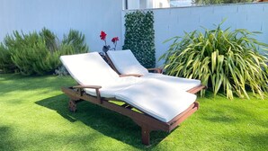 Un fauteuil de jardin en bois avec des coussins blancs, placé dans un espace verdoyant bien entretenu.