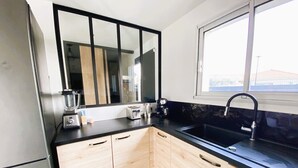 Une cuisine moderne avec un plan de travail noir, des meubles en bois, un grand miroir et une fenêtre.
