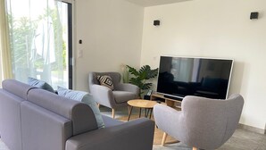 Un salon moderne avec un canapé gris, un fauteuil gris, une petite table ronde et un grand téléviseur à écran plat.