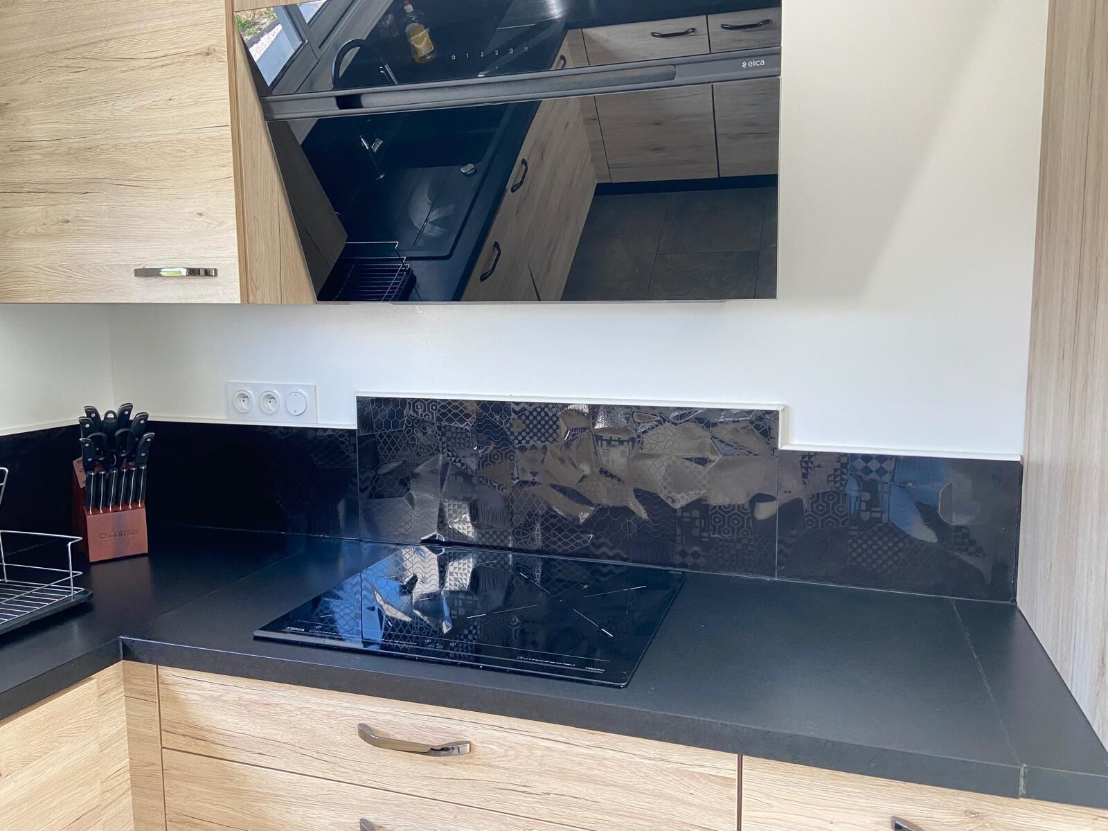 Une cuisine moderne dotée d’une plaque de cuisson à induction noire, de meubles en bois et d’un crédence ornée d’un motif géométrique.