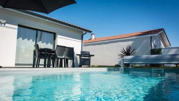 Une maison moderne dotée d’une piscine, de mobilier d’extérieur et d’un grand parasol.