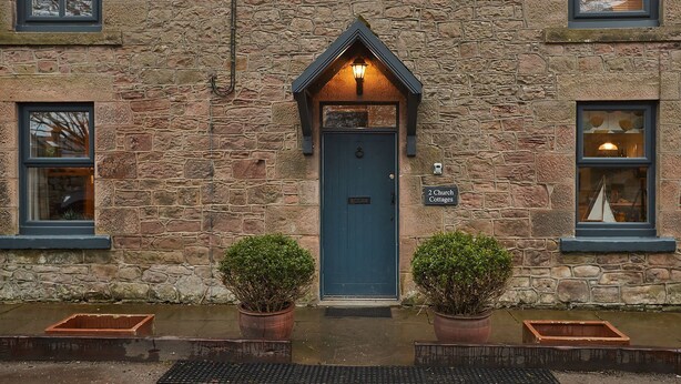 A stone building with a dark blue door, two potted plants, and a sign indicating '2 Church Cottages'. - Church Cottage Beadnell  (Beadnell)