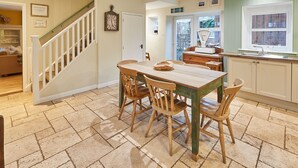 A dining area with a wooden table and chairs, a staircase, and a kitchen with a window. - Church Cottage Beadnell  (Beadnell)