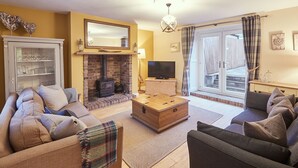 A living room with a fireplace, sofas, a television, and a large window with curtains. - Church Cottage Beadnell  (Beadnell)