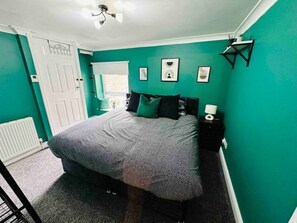 Cozy retreat with a comfortable bed, a window with blinds, and a convenient table with a lamp.