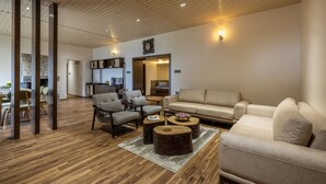 A spacious living room with a wooden floor, a beige sofa, and a dining area with chairs and a table.