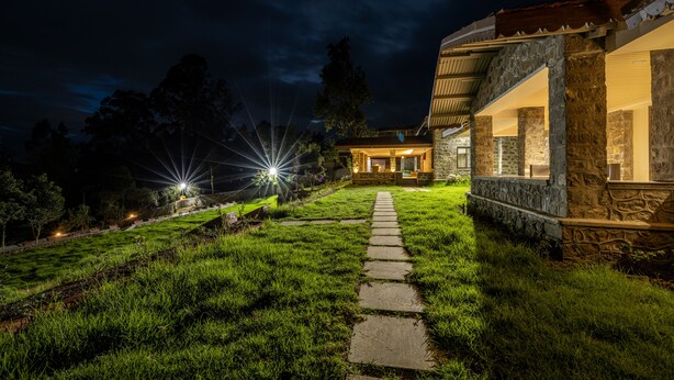 A stone house with a stone pathway leading to the entrance, surrounded by a grassy area and trees.