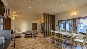 A modern living room with a wooden floor, a sofa, a dining table with chairs, and a TV on a stand.