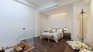 Une chambre moderne avec un lit, des tables de chevet, un banc et une rambarde en verre.