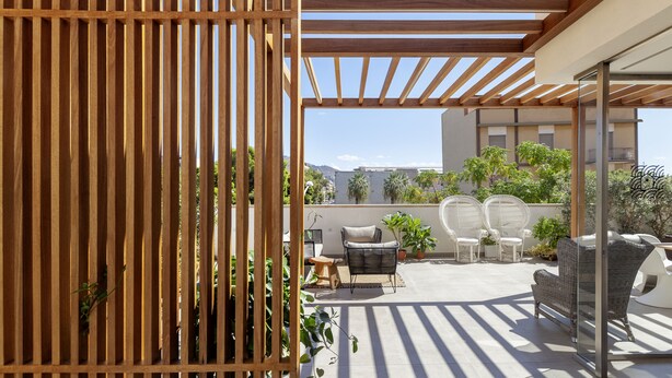 Une terrasse sur le toit agrémentée d’une pergola en bois, de meubles en osier et de plantes en pot.