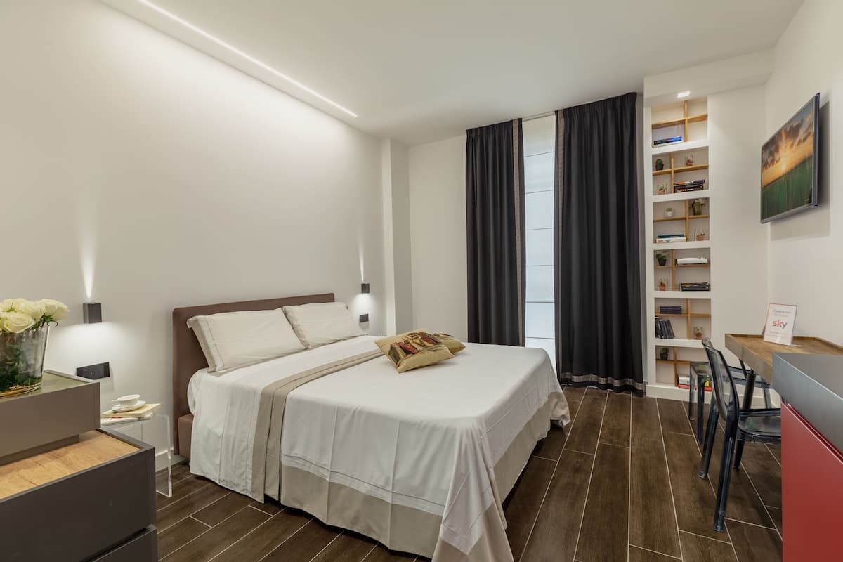 Moderni hotellihuone, jossa on suuri sänky, työpöytä ja kirjahylly.