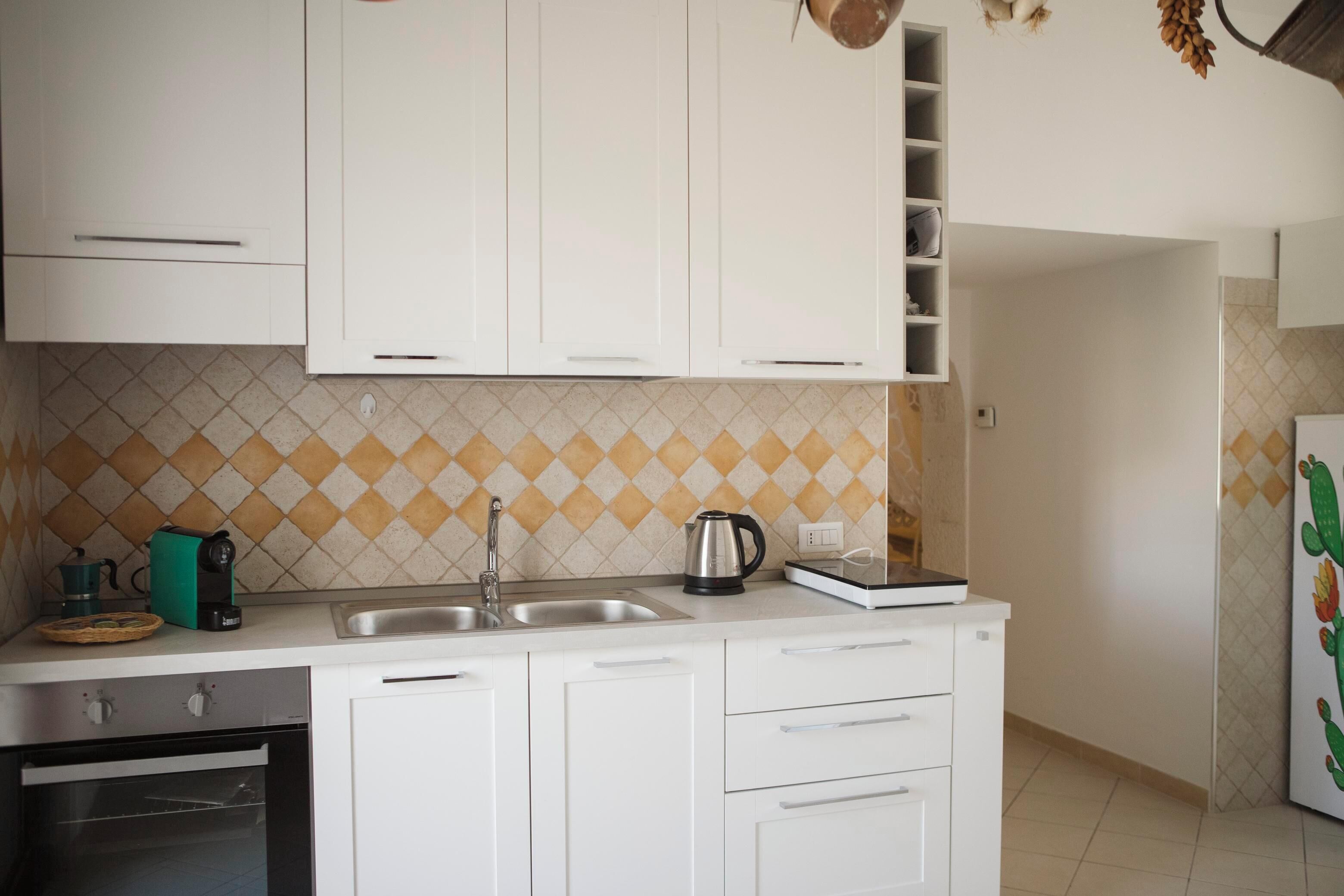 Een keuken met witte kastjes, een gootsteen, een waterkoker en een koffiezetapparaat.