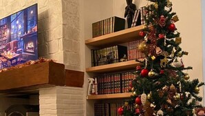 Una sala de estar acogedora con chimenea, un árbol de Navidad y una estantería llena de libros.