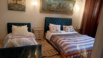 A bedroom with two beds, a nightstand, a dresser, and a painting on the wall.