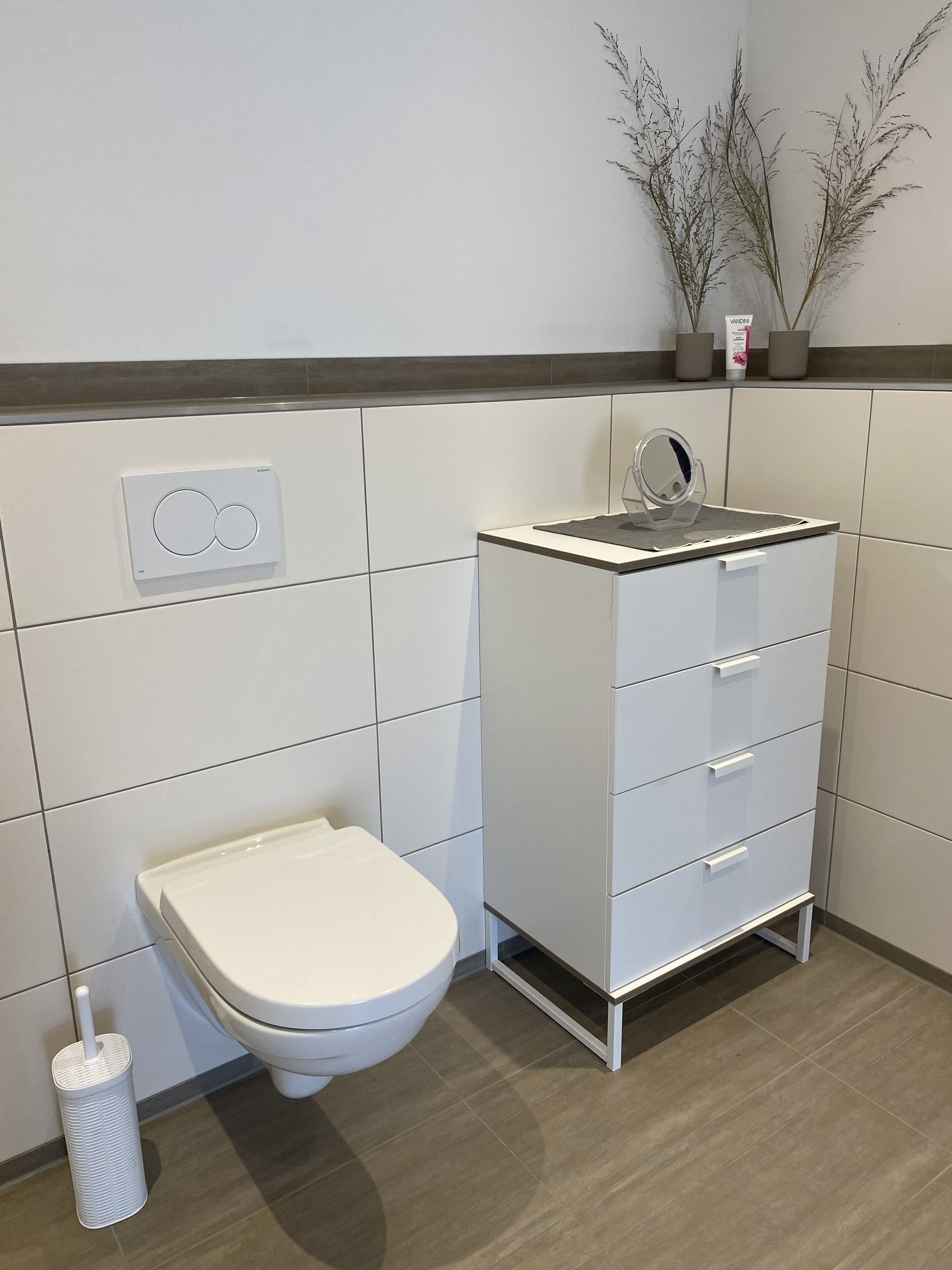 Un baño moderno con inodoro, tocador con cajones, espejo y panel de control en la pared.