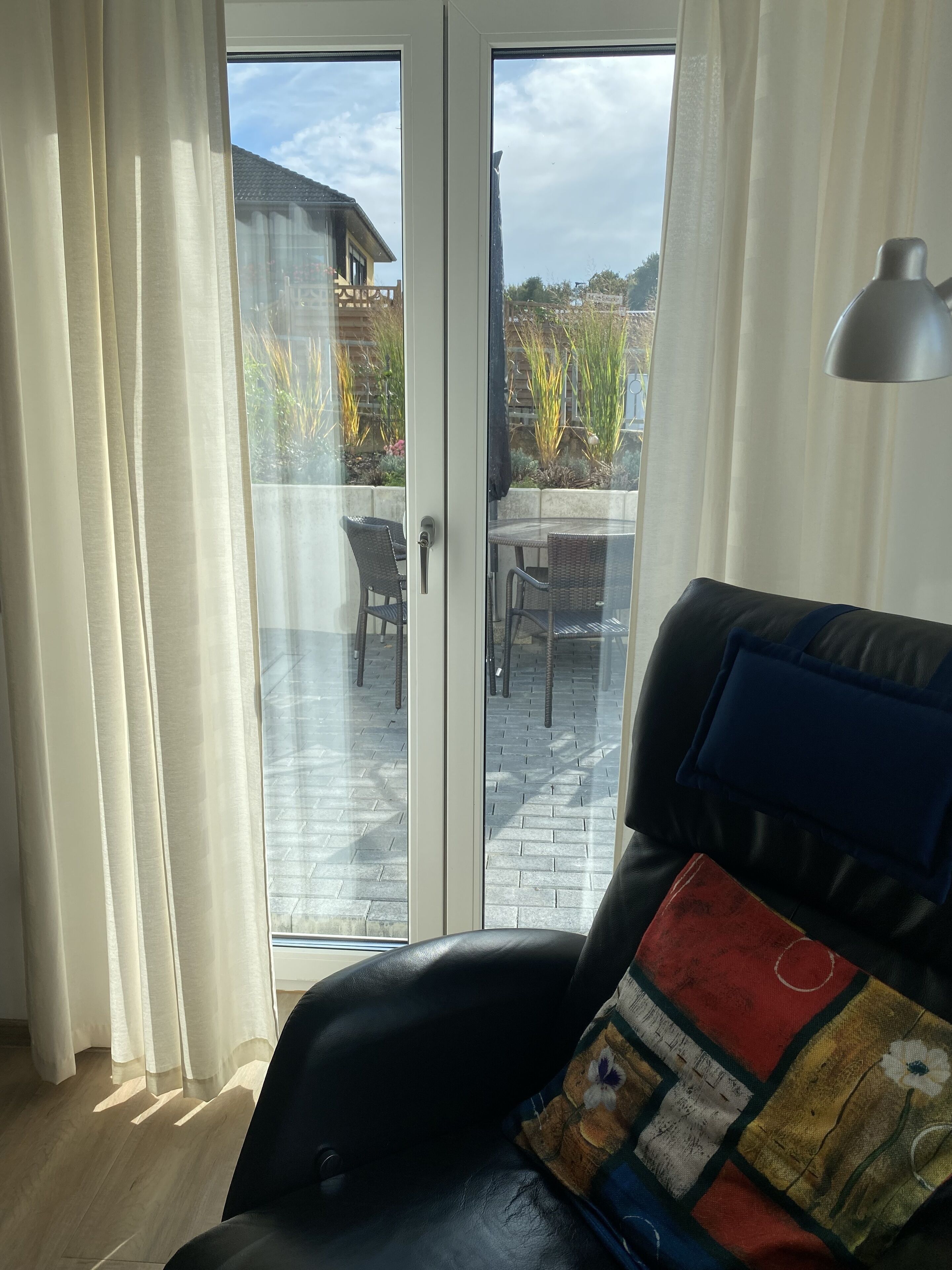 A room with a black leather sofa, a glass door leading to an outdoor patio, and a metal lamp.