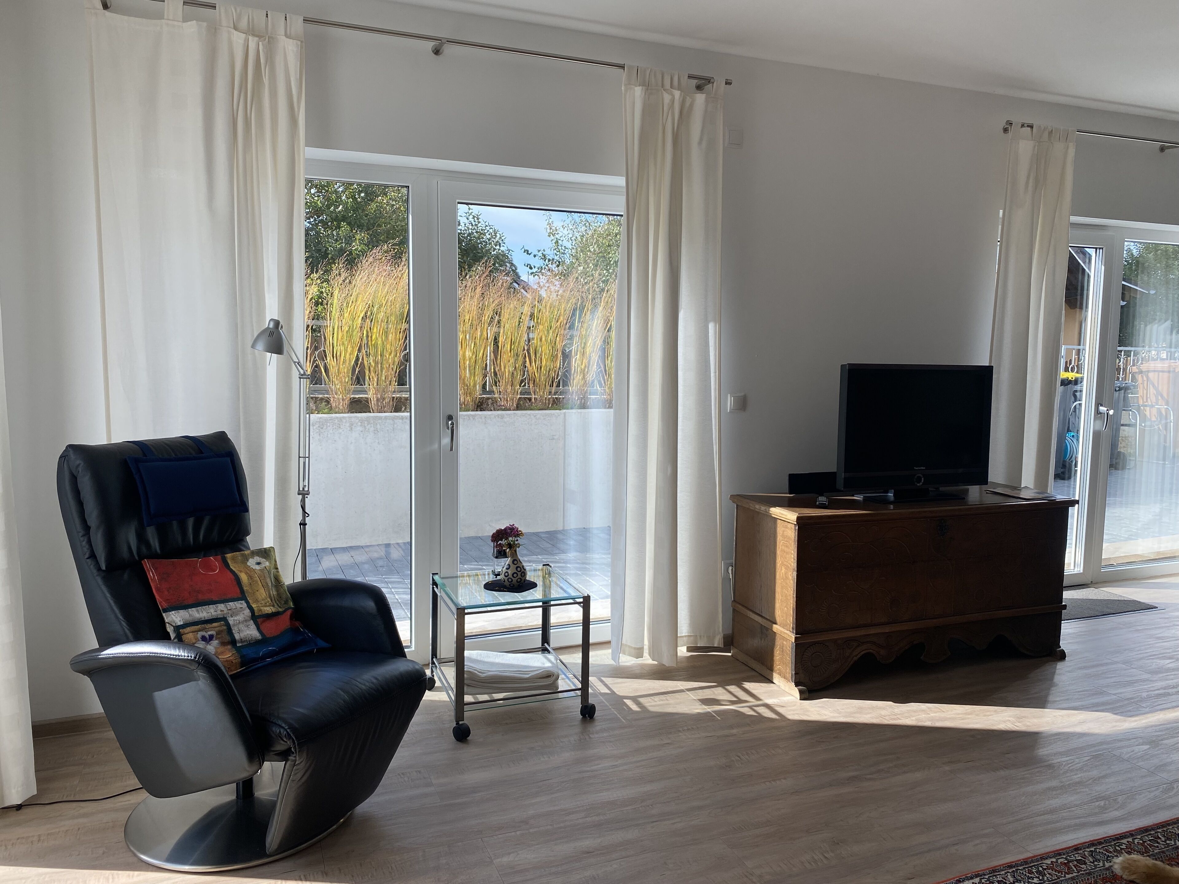 Ein modernes Wohnzimmer mit Ledersessel, Glastisch, Holzschrank und Fernseher.