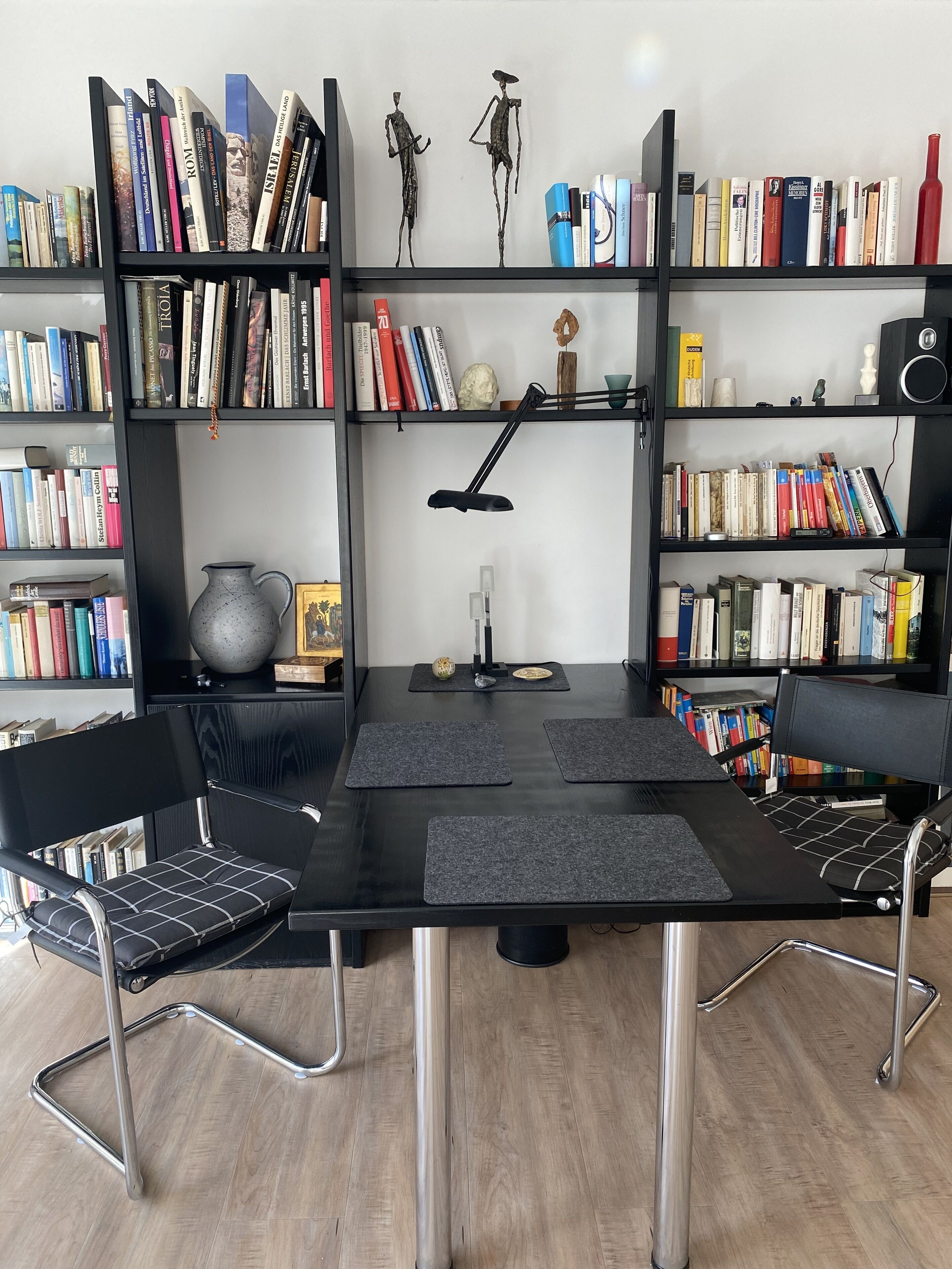 Ein Lernbereich mit einem schwarzen Schreibtisch, zwei schwarzen Stühlen, einer schwarzen Schreibtischlampe und mehreren Bücherregalen voller Bücher.