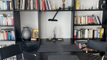 Ein Lernbereich mit einem schwarzen Schreibtisch, zwei schwarzen Stühlen, einer schwarzen Schreibtischlampe und mehreren Bücherregalen voller Bücher.