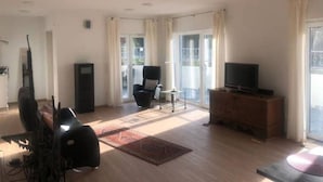 Amplia sala de estar con televisión de pantalla plana, un sofá, una silla y una mesita.