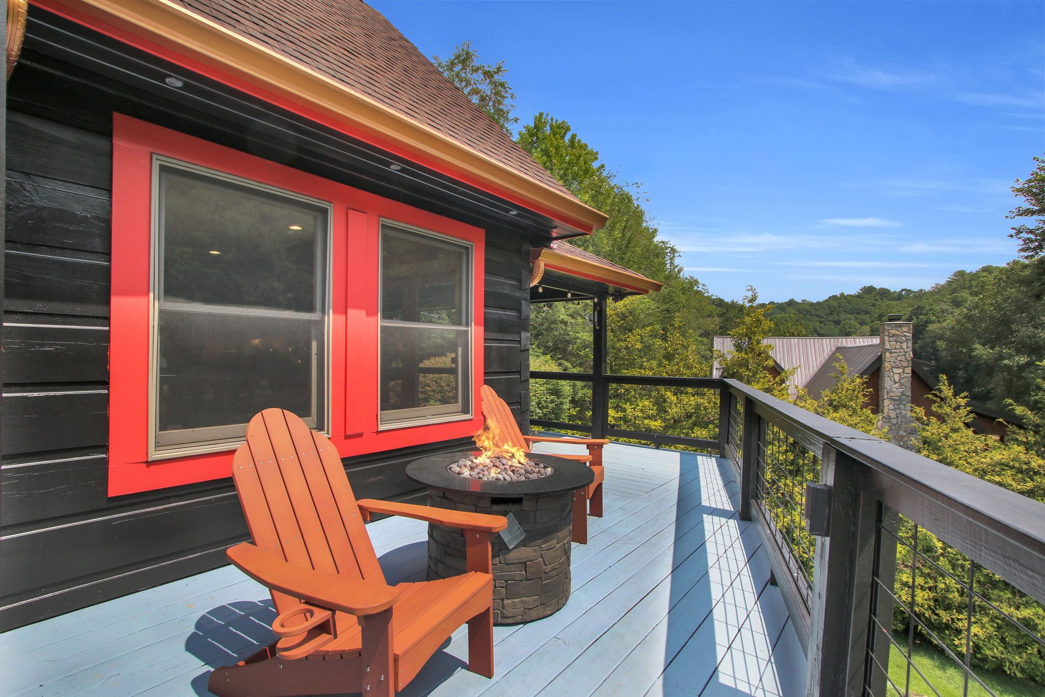 A deck with a fire pit and Adirondack chairs, overlooking a forested area.