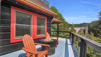 A deck with a fire pit and Adirondack chairs, overlooking a forested area.