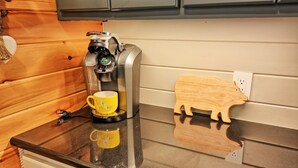 A coffee maker on a countertop with a yellow mug and a wooden pig-shaped coaster.