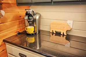 A coffee maker on a countertop with a yellow mug and a wooden pig-shaped coaster.