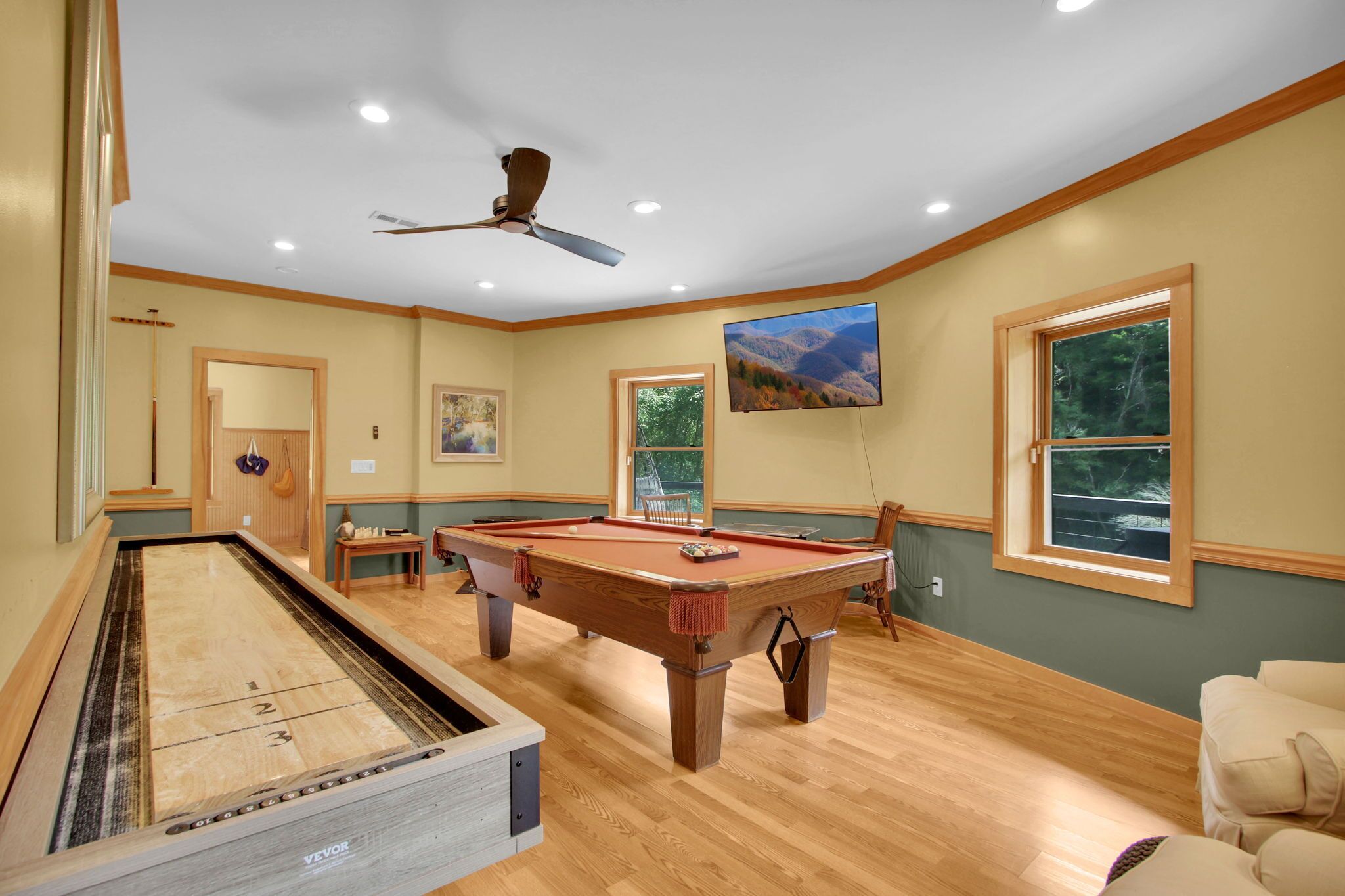 A pool table in a room with wooden flooring, a ceiling fan, and a painting on the wall.