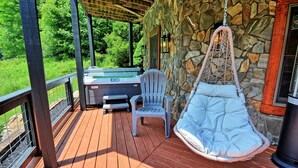 A wooden deck with a hot tub, a chair, and a hanging chair.