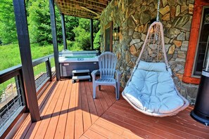 A wooden deck with a hot tub, a chair, and a hanging chair.