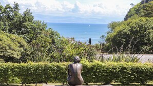 A sculpture of a seated figure in a garden with a view of the sea and mountains. - Pennant Igyn (Pwllheli)