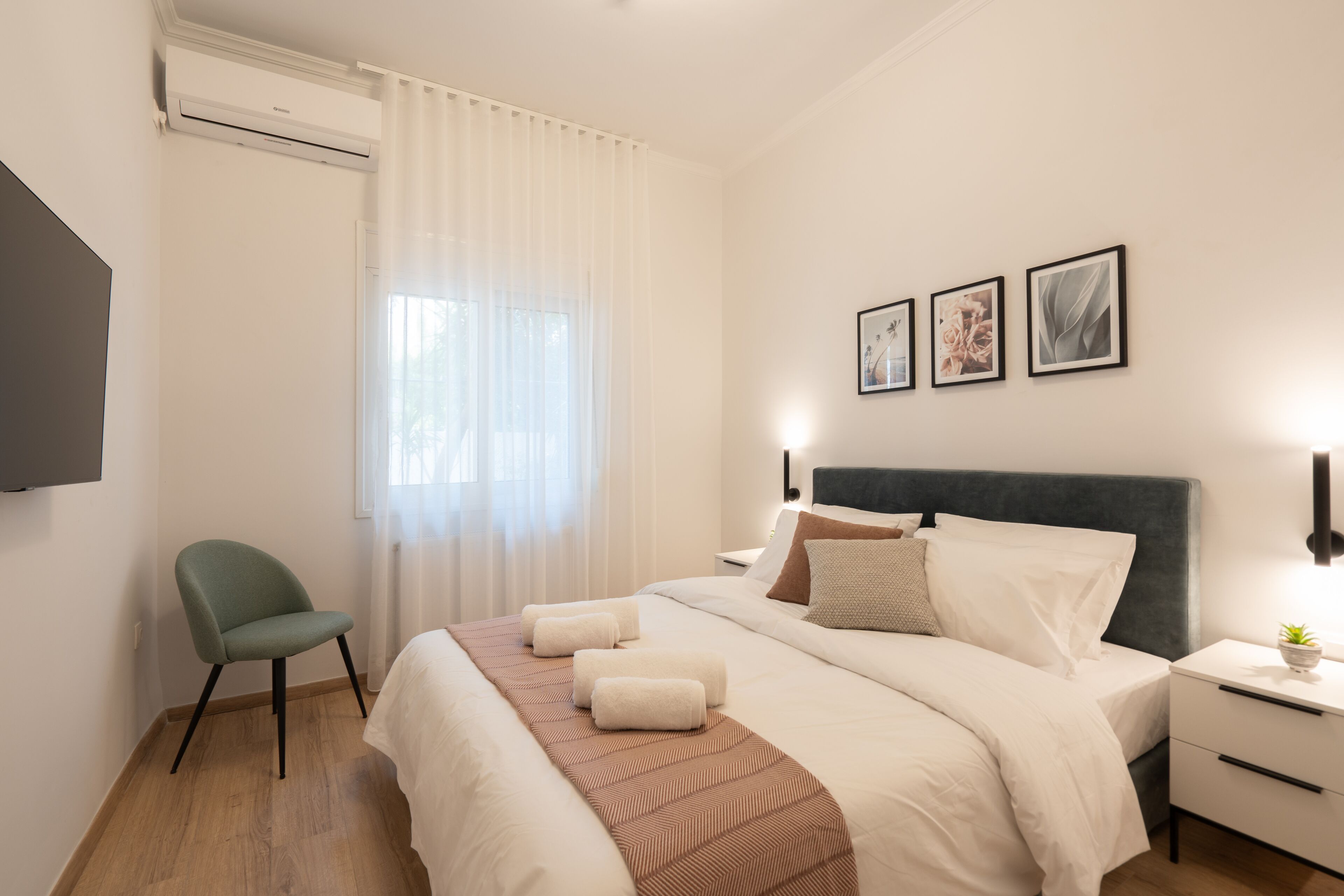 A hotel room with a bed, a chair, a bedside table with a lamp, and a wall-mounted TV.