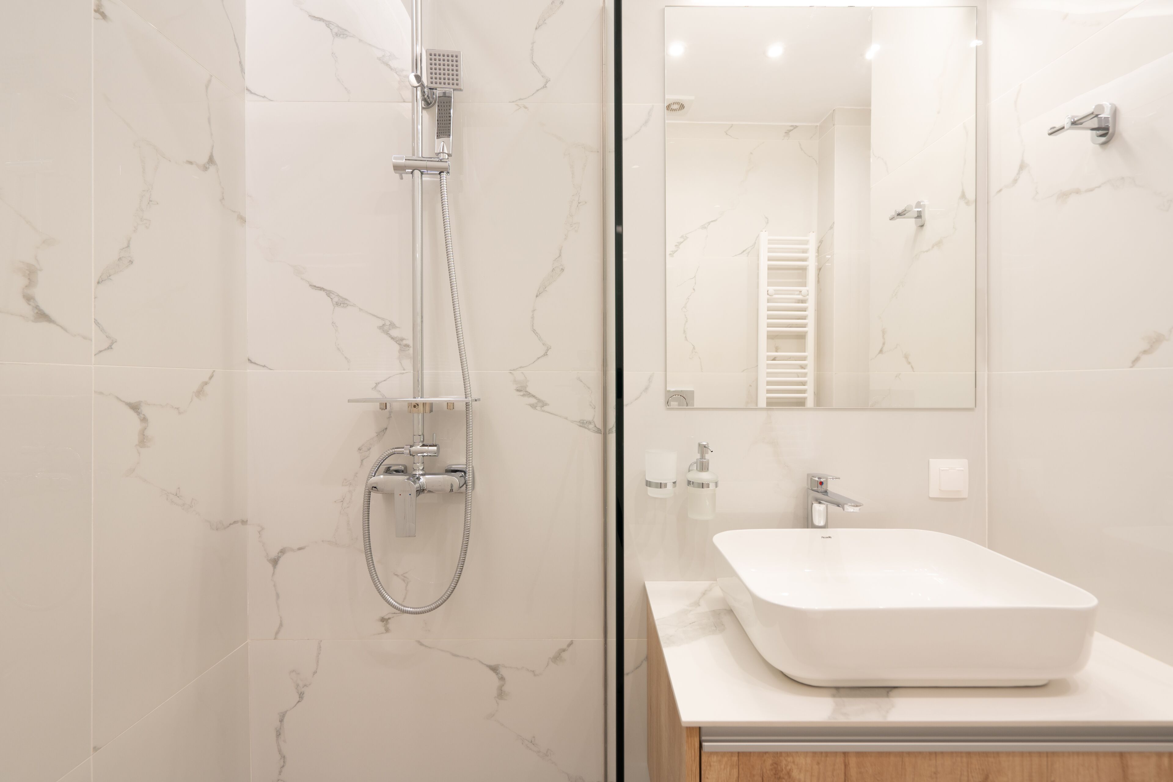 Un baño moderno con pared de mármol, ducha con mampara de cristal, lavabo blanco y espejo.