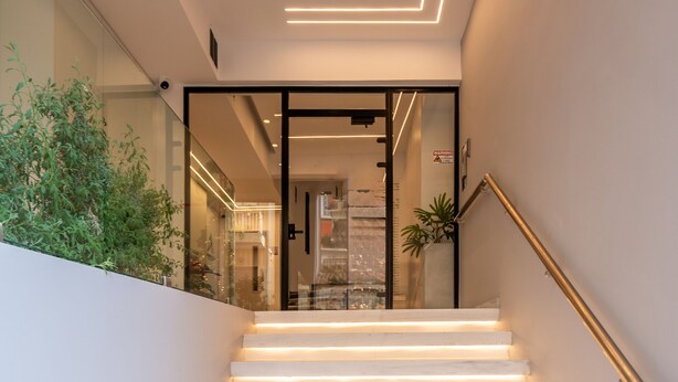Una escalera moderna con peldaños blancos y barandilla de vidrio, que lleva a una habitación con vistas a la ciudad.