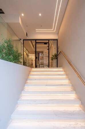 Una escalera moderna con peldaños blancos y barandilla de vidrio, que lleva a una habitación con vistas a la ciudad.