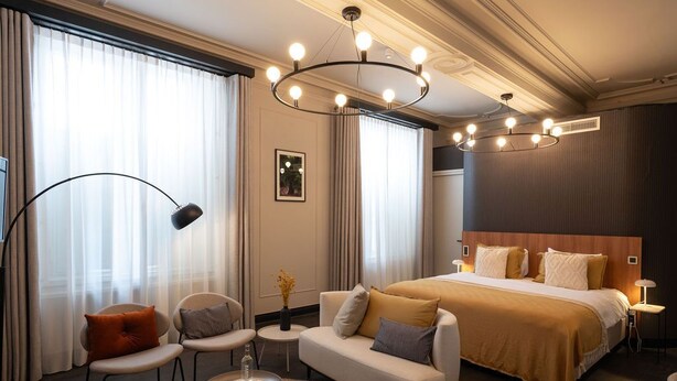 A hotel room with a large bed, a sofa, two chairs, a small table, and a floor lamp. - Hotel Kint (Valkenburg aan de Geul)