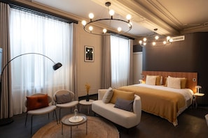 A hotel room with a large bed, a sofa, two chairs, a small table, and a floor lamp.